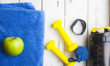 Diyet Zayıflama kilo kaybı kavramı zamanı. Spor, fitness, elma, spor ayakkabıları, şişe su ve sarı ağırlık beyaz ahşap zemin üzerinde