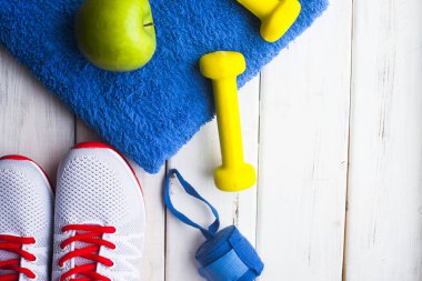 Diyet Zayıflama kilo kaybı kavramı zamanı. Spor, fitness, elma, spor ayakkabıları, şişe su ve sarı ağırlık beyaz ahşap zemin üzerinde