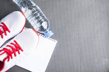 Diyet Zayıflama kilo kaybı kavramı zamanı. Spor, fitness, elma, spor ayakkabı, şişe su ve sarı ağırlıkları gri kauçuk zemin üzerine