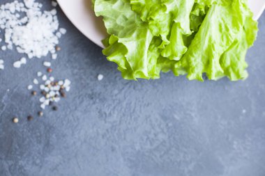 Heathy gıda vejetaryen kavramı. Bir tabak ve kopya alanı, üstten görünüm karanlık bir beton zemin üzerine tuz taneleri marul yaprakları