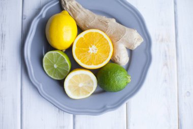 Sağlıklı yemek, çay, soğuk tedavi kavramı. Yeşil limon, limon ve zencefil kökü bir mavi tabak, Beyaz ahşap zemin, üstten görünüm