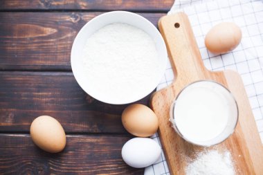 Homamde pasta, pastane kavramı. Buğday unu, tavuk yumurtası ve bir bardak taze organik süt, kesme tahtası, beyaz peçete ve koyu renk ahşap arka plan olarak bir kase