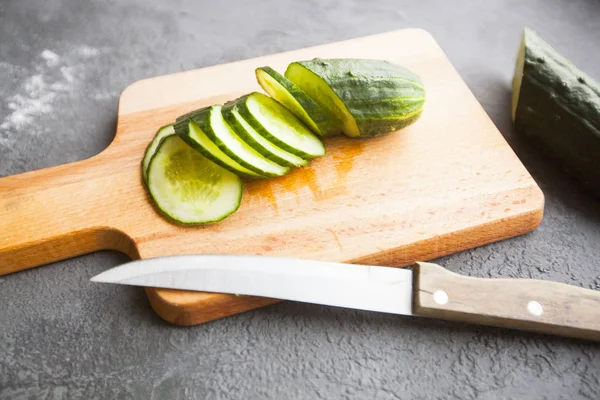 Heathy food Vegetarian Concept. Cutting a fresh cucumber on a wooden board, dark concrete background with copy space, top view