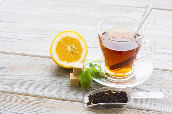 Black tea ceremony - glass full of tea, tea leaves, sugar, yellow lemon, spices on a wooden boards background. Top view