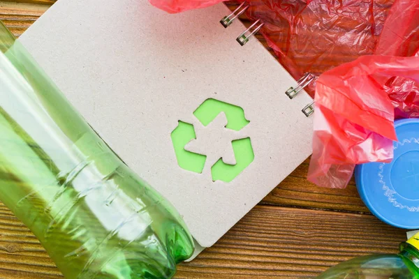 Environmental protection, ecology and recycling concept, recycle sign, notepad and garbage on dark wooden background top view closeup