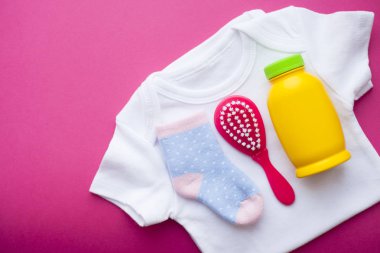 Yeni doğmuş bebek hikayesi. T-shirt ve çocuk oyuncakları, makas, bebek şişesi, meme, kırmızı arka plan üzerinde saç fırçası