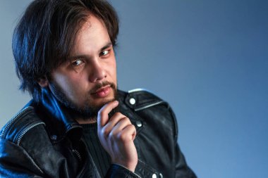Rock tarzı veya bisikletçinin Tema. Sakallı bir siyah deri ceketli siyah saçlı bir adam portresi elini çenesine üzerinde tutar. Mavi arka plan.