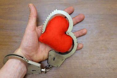Bir adamın elinde kırmızı yumuşak kalp ile gerçek çelik polis kelepçe kahverengi bir arka plan üzerinde zincirle. Aşk ve hukuk, kalp hastalığı kavramı.