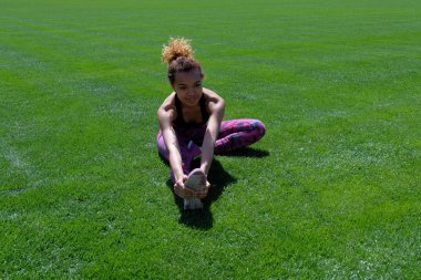 Güzel siyah sporcumuz ile yeşil çim sahada germe yapıyor. Uzay kopyalayın. Yaşam tarzı.