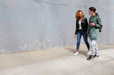 Siyah bir kız ve bir beyaz adam, el ele tutuşarak ve gri, eski püskü doku duvar eski cadde boyunca yürüyüş bakıyoruz. Uluslararası Gençlik modern yaşam tarzı. Kopya alanı için grafiti.