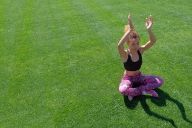 Güzel bir genç Afro-Amerikan kız siyah T-shirt ve pembe spor ayakkabı yoga yeşil çimenlerin üzerinde çalışmaktadır ve ellerini yukarı yükseltir. Modern spor yaşam tarzı. Kopya alanı.