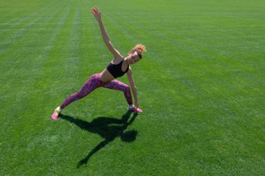 Modern tarzı yaşam. Afrikalı-Amerikalı kız siyah T-shirt, pembe pantolon ve spor egzersizleri yeşil çimenlerin üzerinde yapıyor ve elleri kadar yükselterek spor ayakkabı. Kopya alanı.