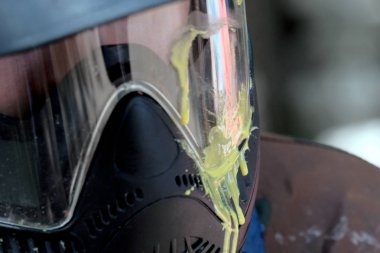 Headshot. Paintball oynamak için koruyucu cam maske üzerinde boya sarı leke Close-up. Sığ derinlik-in tarla. Bulanık.