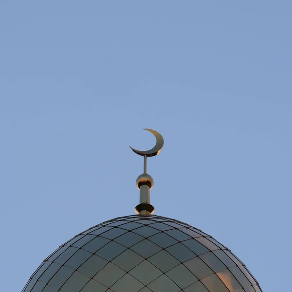 The symbol of Islam is a golden crescent moon on top of the mosque minaret on the blue evening of the morning sky. A square picture.
