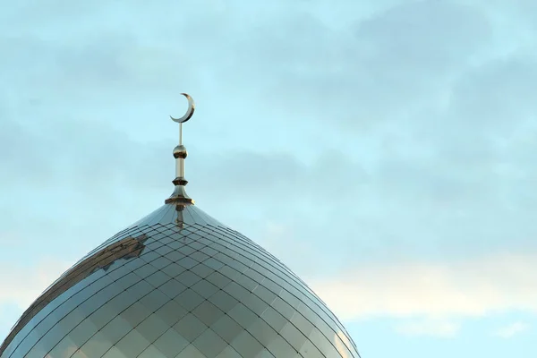 The symbol of Islam is a golden crescent moon on top of the mosque. Minaret on the blue morning sky with clouds.