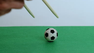 Erkek el yakın çekim için Çince veya Japonca gıda yemek çubukları ile harekete geçiren ve bir futbol topu üzerinde yeşil bir alana düşürür. Asya Futbol kavramı. Kopya alanı.