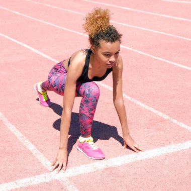 Bir genç güzel esmer kız sportif siyah T-shirt ve pembe spor ayakkabı Stadyumu başlangıç çizgisine yanındaki yeşil çim yarış hazırlanıyor. Kare resim. Yaşam tarzı.