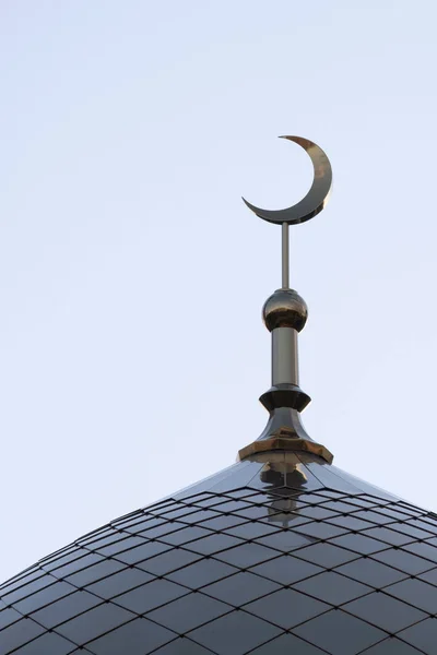 The top of the mosque minaret. The symbol of Islam is a golden crescent moon on a blue evening or morning sky. Vertical picture.