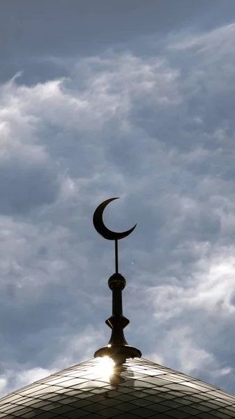 Vertical shot. The symbol of Islam is a golden crescent moon on top of the mosque minaret on the blue evening of the morning sky with clouds.