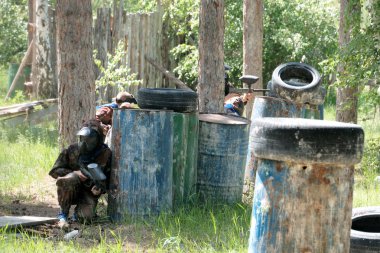 Paintball oynamak için ormana çöplük alan. Siyah koruyucu maskeler ve Kamuflaj giysileri oyuncular arasında ağaçlar, çim elinde silah ile bir ekip varil ve lastikleri.