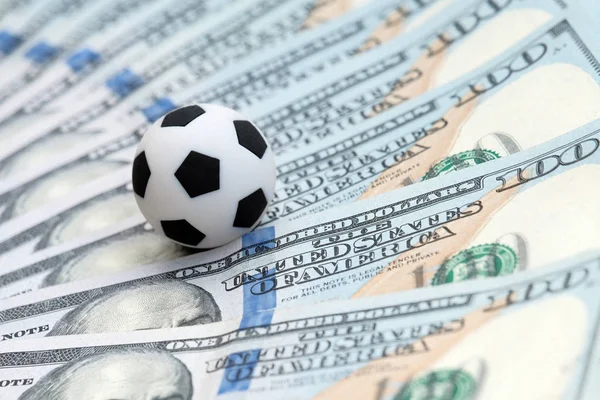 Futbol topu küçük bir yüz dolarlık banknot üzerinde yalan. Para ve futbol topu - spor ve iş arka plan.