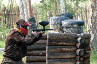 İçinde paintball oynarken. Bir kız ya da bir adam bir yüz maskesi ve kamuflaj üniforma ellerinde silahla düşman nedeniyle ahşap barınak hedefliyor.