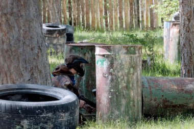 Spor oyunu paintball. Kamuflaj giysili bir adam elinde silah ile dışarı bir demir namlu arkasından iletiye göz atar.