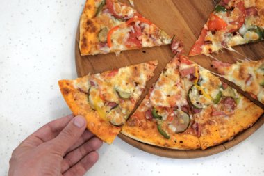 Bir adamın elinde bir parça pizza ahşap plaka alır. Beyaz masa artalanını. Yukarıdan görüntülemek.