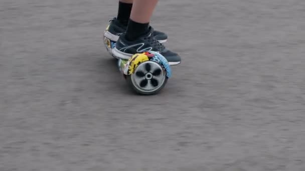 Primer plano de un hombre piernas en zapatillas de deporte en un auto-equilibrio de dos ruedas de transporte por carretera. Hoverboard graffiti de color se mueve a lo largo del asfalto . — Vídeos de Stock