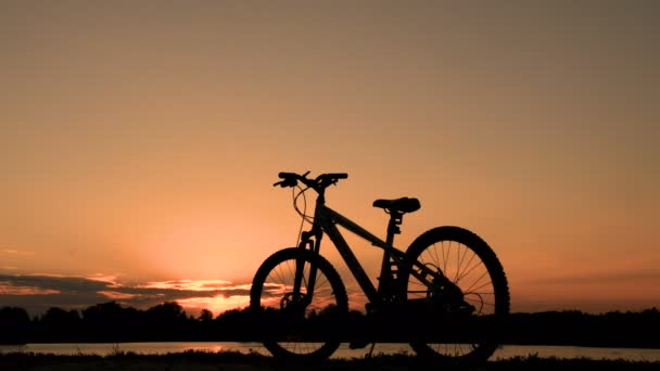Una bicicleta solitaria se para en el paseo marítimo. Un adolescente al amanecer se acerca a la bicicleta y se va en ella . — Vídeos de Stock