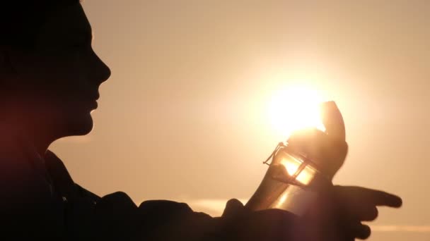 一个青少年的轮廓对太阳的剪影 那家伙打开一个运动瓶 通过管子喝水 复制空间 — 图库视频影像