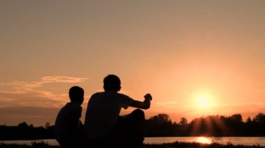 Baba ve oğul Rıhtımlar üzerinde oturan ve gündoğumu veya günbatımı dikkat et. İki kişi bir nehir ya da göl kıyısında iletişim silüeti.