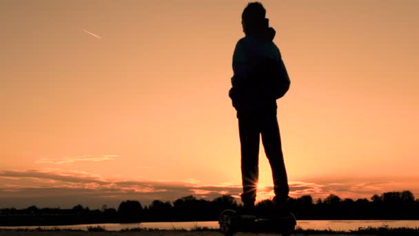 一个十几岁的小伙子在日出时沿着河边开着两轮的自我平衡 Hoverboard 健康的生活方式 — 图库视频影像