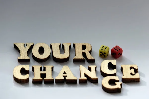 The inscription YOUR CHANCE, CHANGE from wooden letters and two dice of red and yellow on a white background. Concept of luck in the game.