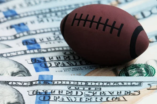 Rugby veya ABD'de yüz dolar faturaları bir arka plan üzerinde Amerikan futbolu sembolü Close-up. Bozulması veya spor bahisleri kavramı.