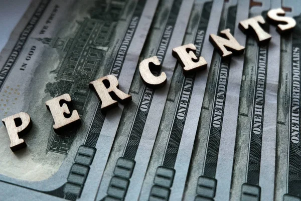 The concept of financial transactions and bank loans. The word PERCENTS is lined with wooden letters on the background of hundred-dollar bills.