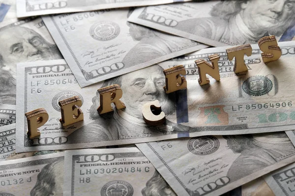 The concept of financial transactions and bank loans. The word PERCENTS is lined with wooden letters on the background of hundred-dollar bills.