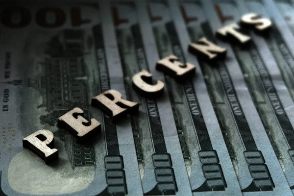 The concept of financial transactions and bank loans. The word PERCENTS is lined with wooden letters on the background of hundred-dollar bills.