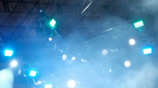 Concert light and smoke in the rain. Bright yellow and blue beams of searchlights on the stage. Blurry. Background footage. — Stock Video