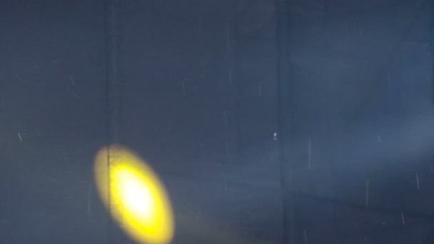 Raggi di luce e macchie gialle da luci da concerto su tessuto nero. Pioggia durante uno spettacolo o una celebrazione in strada . — Video Stock