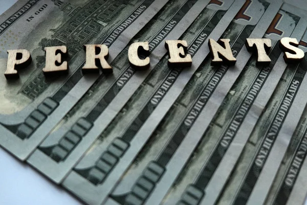 The concept of financial transactions and bank loans. The word PERCENTS is lined with wooden letters on the background of hundred-dollar bills.