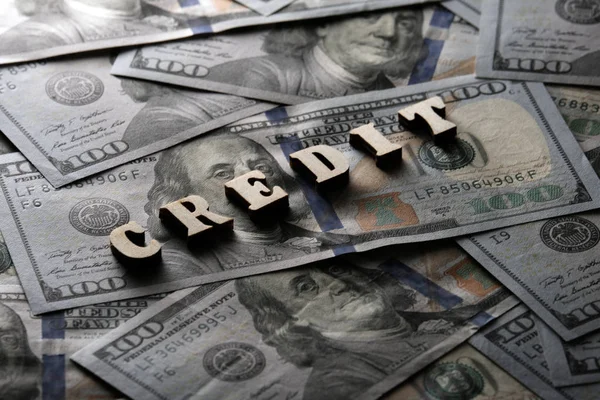 The concept of financial transactions and bank loans. The word CREDIT is lined with wooden letters on the background of hundred-dollar bills.
