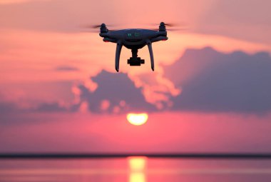 Radyo kontrollü dron günbatımı su yüzeyi üzerinde silüeti. İnsansız hava aracı arka plan pembe bulutlar üzerinde. Göksel fotoğraf ve video kavramı.