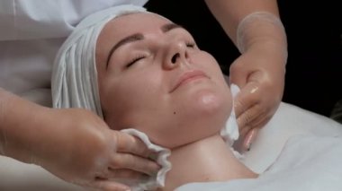 Yakın çekim. Relax beyaz peçete ile eldiven eller temizler yüz ve boyun güzel bir kız. Karboksiterapi güzellik salonda yordamı aşamasıdır.