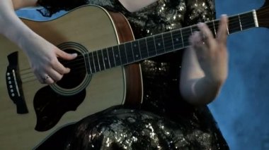 Bir kız bir gece elbisesi içinde altı telli akustik gitar çalar. Sağ el dizeleri dokunursa, sol el akorları klavye üzerinde tutar. Arka planda duman. Gün müzik.