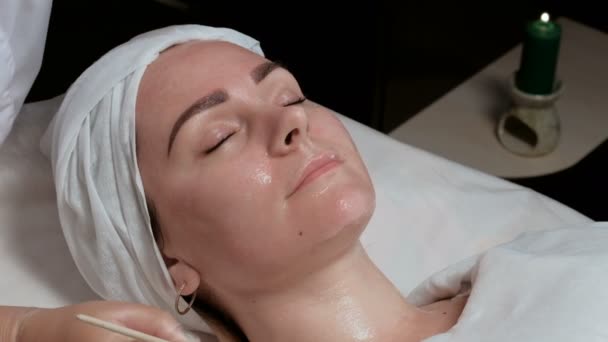 プロの美容師が美容室で女性の首に化粧品のマスクを適用します 美容センターでクライアントの顔ブラシで透明なゲルを適用するための手順 — ストック動画