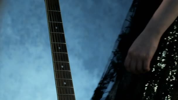 フォア グラウンドでギターのフレット ボード コンサート ドレスの女の子がやってきて優しく彼女の手を文字列に通過 音楽の日のテーマ — ストック動画