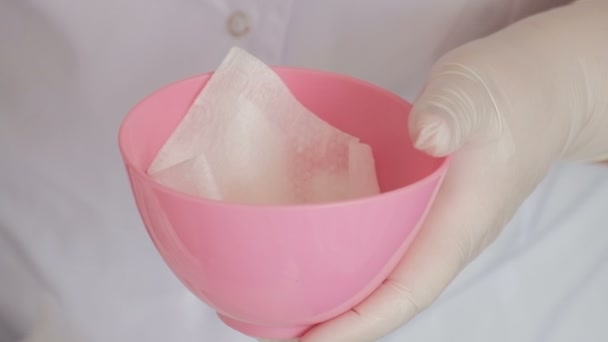 Tema de cosmetología o medicina. Primer plano de las manos femeninas con guantes blancos vertiendo un líquido transparente en una taza de goma rosa . — Vídeos de Stock