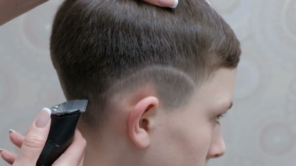 Un moderno peinado adolescente en una peluquería. Un primer plano de las manos de un peluquero que se afeita una tira sobre la oreja de un joven con un cortador de pelo . — Vídeo de stock