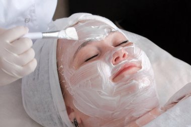 Şişman bir kadın temizlik ve Güzellik Salonu'nın ofisinde yüz cilt toparlama bir yordam alır. Güzellik uzmanı eldiven eller bir fırça ile bir kız alnına beyaz krema yayma.